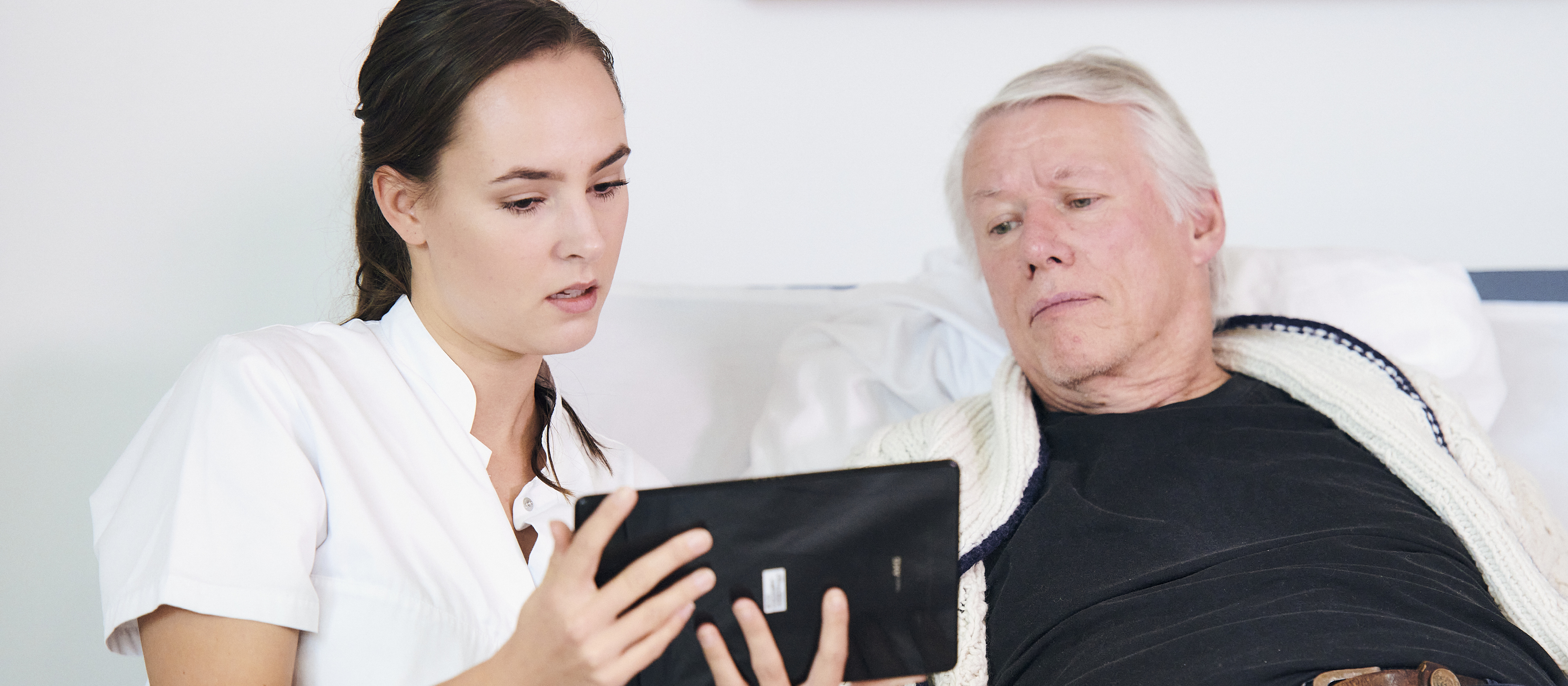 Sygeplejerske viser ipad til sengeliggende mandlig patient